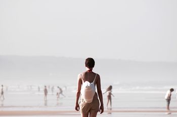 Rear view of woman carrying bag while walking on beach during foggy weather