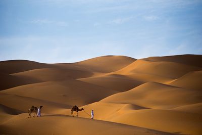 People walking on sand dune in desert against sky