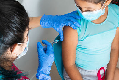 Children's nurse injecting brown girl's arm. doctor's hand with rubber gloves injecting covid-19