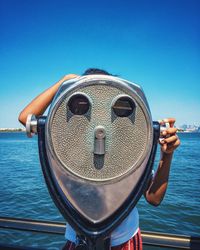 Person looking through coin-operated binoculars by sea at liberty island