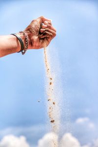 Cropped hand spilling sand against blue sky