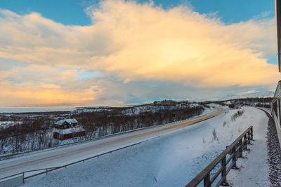 Snow covered road against sky during sunset