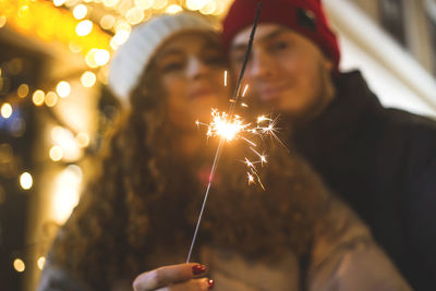 A sparkler burns in the hands of a girl hugged by her boyfriend in a christmas mood.