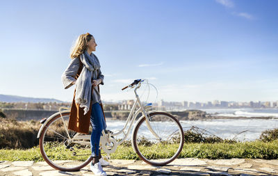 Spain, gijon, smiling young woman on bicycle at the coast