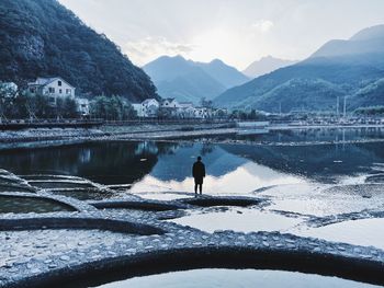 Rear view of person standing by lake against sky during winter