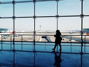 Rear view of woman at airport runway against sky