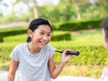 Smiling girl holding badminton racket while standing on footpath