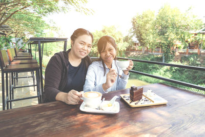 Portrait of smiling mother and daughter holding coffee cups at outdoor cafe