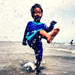 Portrait of happy girl playing in water at beach against sky