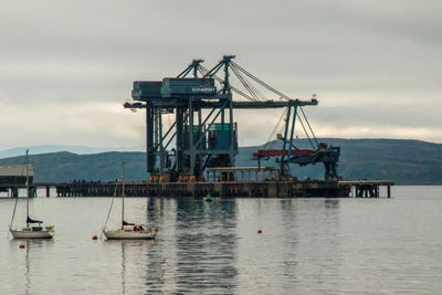 Cranes on pier over sea against sky