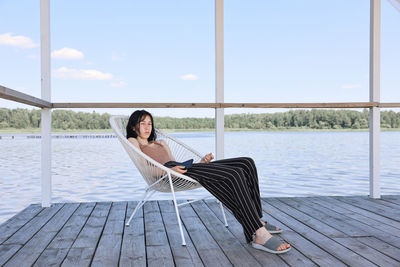 Portrait of young woman sitting on pier over sea against sky