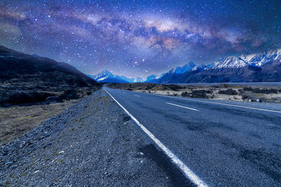 Road by snowcapped mountains against sky at night