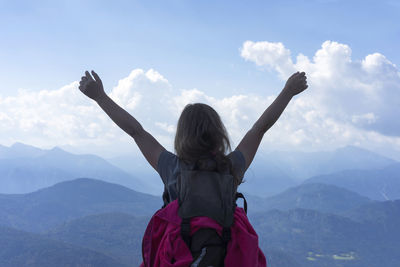 Rear view of female hiker with arms raised against sky at mountain