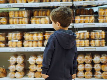 Cute toddler boy in casual clothes in bakery looking at donuts
