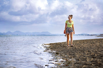Full length of woman standing on beach against sky