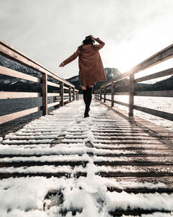 Rear view of woman walking on footbridge during winter