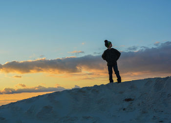 Boy standing on snow covered mountain against sky during sunset