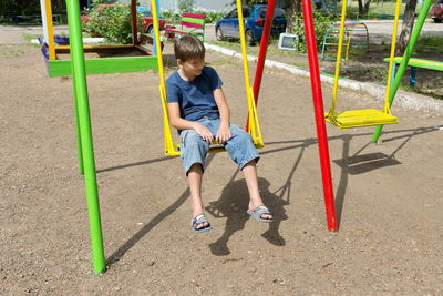 A bored boy sits on a swing in the courtyard of a residential building.