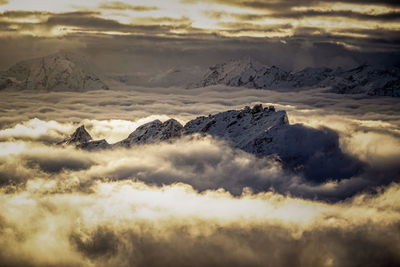 Snow covered mountain peak reaching above a sea of golden clouds at sunset, austria