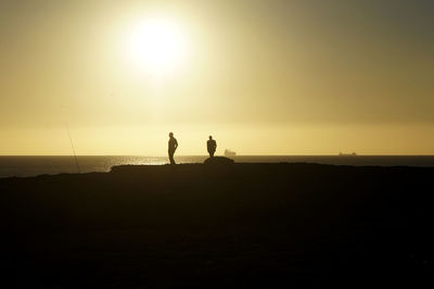 Two silhouette people standing on calm beach