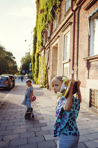 Girls with skateboards on sidewalk by building in city