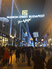 People walking on illuminated street in city at night