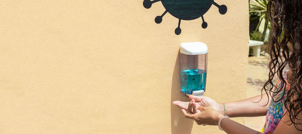 Close-up of woman holding bottle against wall