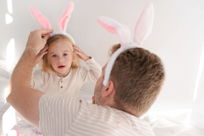 Caucasian man and two years old toddler girl, kid wearing rabbit ears playing with eggs.celebrating 