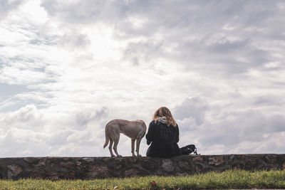 Man with dog sitting on field against sky