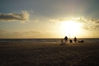 Silhouette people on beach against sky during sunset
