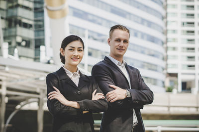 Portrait of business people with arms crossed standing against building in city