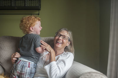 Playful grandmother and grandson sitting on armchair at home