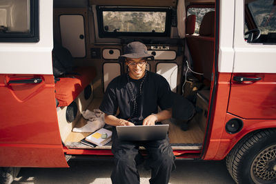 Smiling young man using laptop while sitting in van during road trip