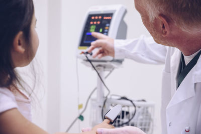 Mature doctor pointing towards monitoring equipment to girl during test in hospital