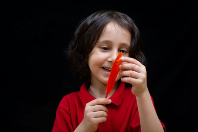 Little boy holding bird feather in hand on black background