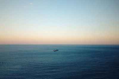 Distance view of boat sailing in sea against sky during sunset