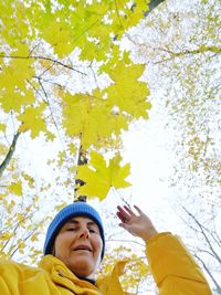 Low angle portrait of smiling young woman standing by autumn leaves outdoors