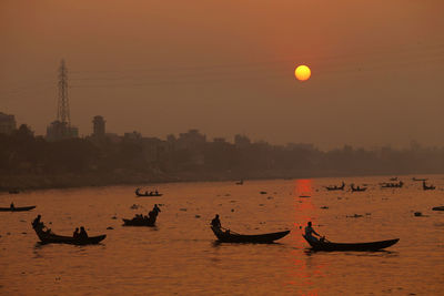 Silhouette people in boat against sky during sunset