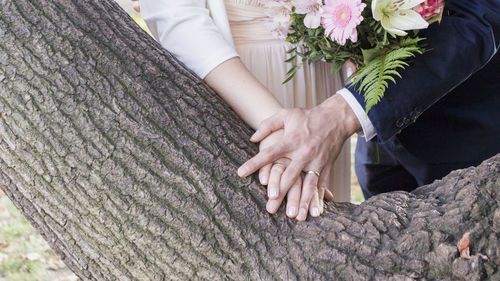 Midsection of bride and bridegroom holding hands by tree