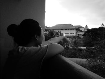 Side view of young woman sitting outside house against sky