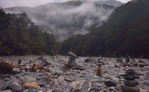 Stack of stones on field by trees in foggy weather