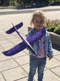 Portrait of cute girl holding purple model airplane