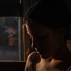 Portrait of a girl in darkness with soft light on her face, pensive silhouette looking down. 