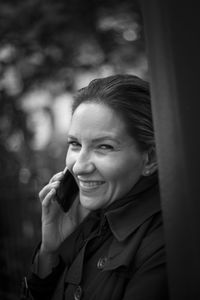 Portrait of smiling woman talking on mobile phone by pole in city