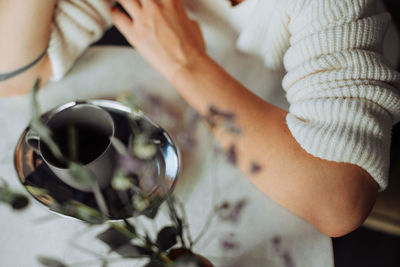 Woman wearing white knitted sweater sitting at table with cup of tea