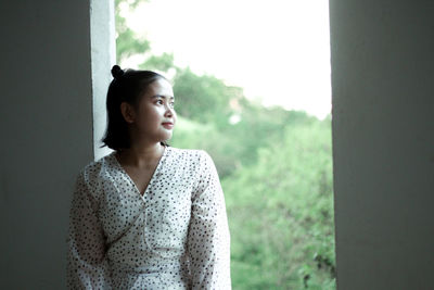 Portrait of young woman standing against trees