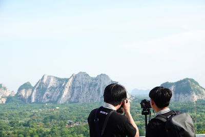 Rear view of people looking at mountains against sky