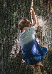 Boy swinging on rope near tree trunk