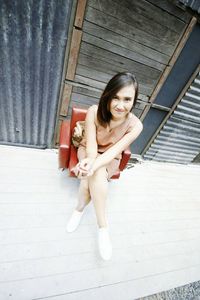 High angle portrait of young woman sitting on chair at porch
