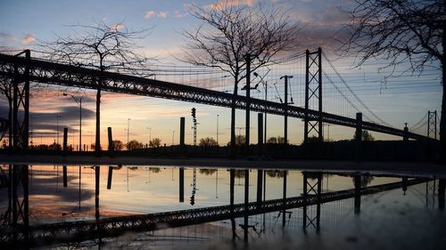 Silhouette bridge over calm river at sunset